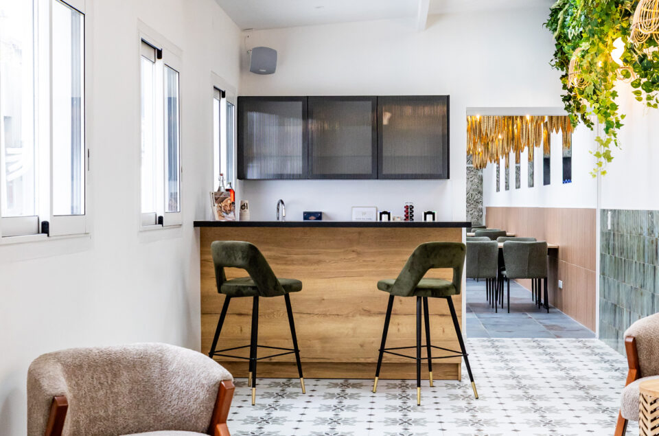 Le Salon Alcia. Vision directe du bar en bois avec ses grands fauteuils kaki en velours. En premier plan fauteuils beige avec petites tables pour s'asseoir