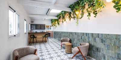 Le Salon Alcia. Vision directe du bar en bois avec ses grands fauteuils kaki en velours. En premier plan fauteuils beige avec petites tables pour s'asseoir