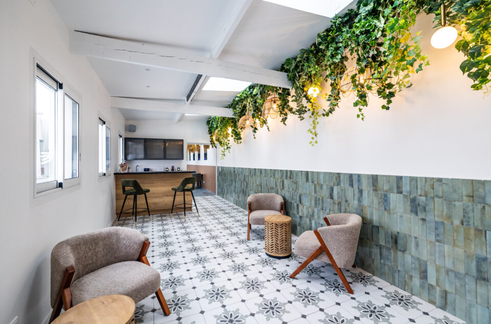 Le Salon Alcia. Vision directe du bar en bois avec ses grands fauteuils kaki en velours. En premier plan fauteuils beige avec petites tables pour s'asseoir