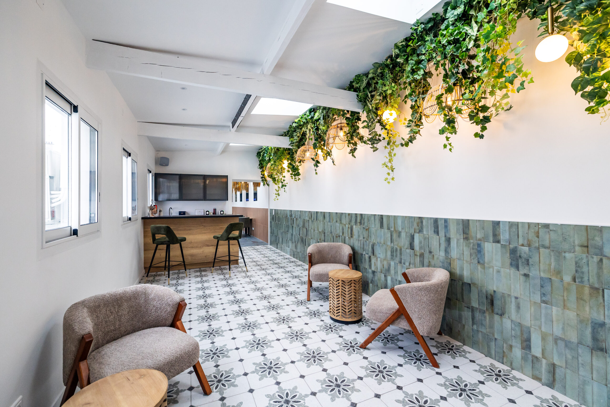 Le Salon Alcia. Vision directe du bar en bois avec ses grands fauteuils kaki en velours. En premier plan fauteuils beige avec petites tables pour s'asseoir