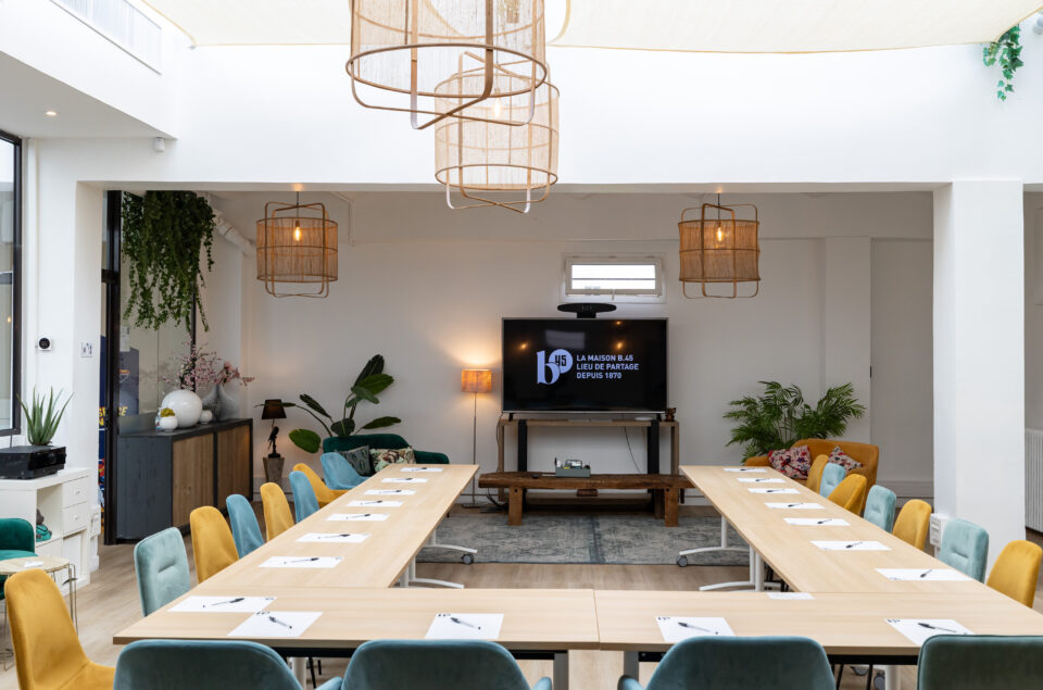 Loft Eiffel avec table en formation U. Feuilles et stylo sur chaque place. Lustre au plafond. vue sur la télé accrochée au mur