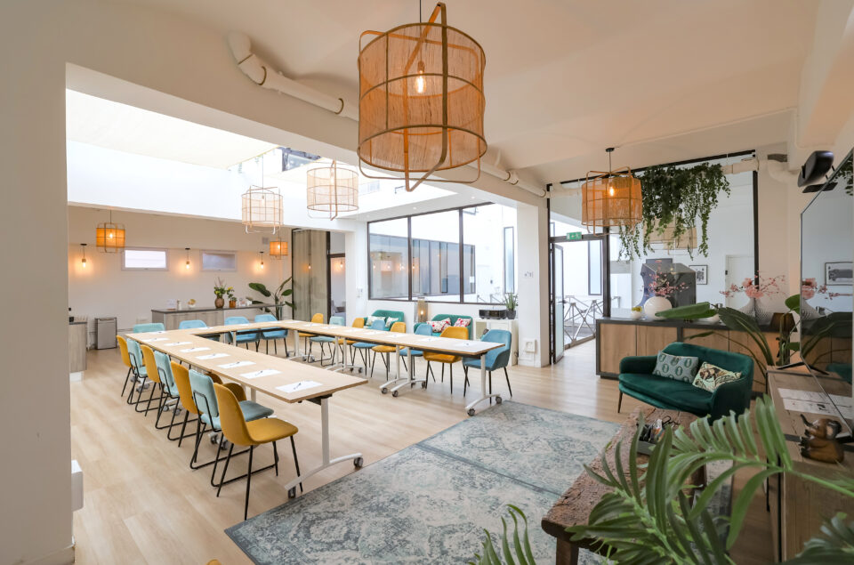 Loft Eiffel avec table en formation U. Feuilles et stylo sur chaque place. Lustre au plafond. Canapé sur les cotés