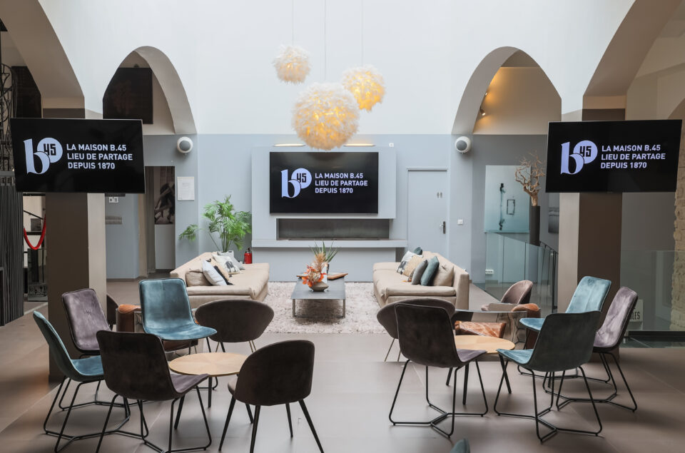 3 télévisons du Grand Loft avec canapé de part et d'autre de cette du milieu accrochée au mur. Chaises et tables basse au fond