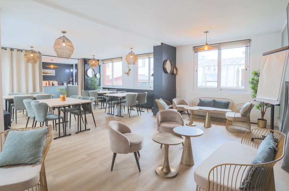 Loft Eden, avec ameublement. En premier plan, des fauteuils et table basse et en arrière plan des tables avec fauteuils effet moumoute grises