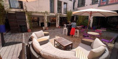 Vue de la Cour avec canapé en demi cercle en premier plan et parasol pour couvrir les tables et chaises