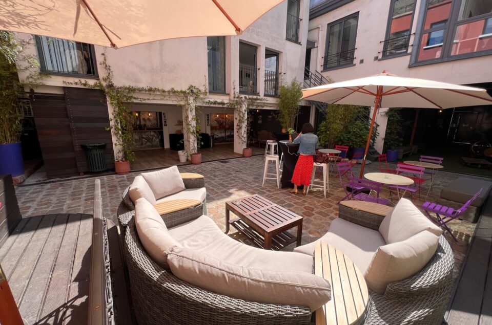Vue de la Cour avec canapé en demi cercle en premier plan et parasol pour couvrir les tables et chaises