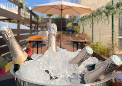 Premier plan seau de champagne rempli de glaçon sur le rooftop et seconde plan parasol et table