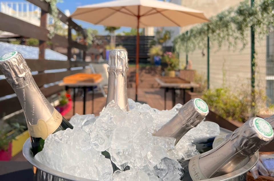 Premier plan seau de champagne rempli de glaçon sur le rooftop et seconde plan parasol et table