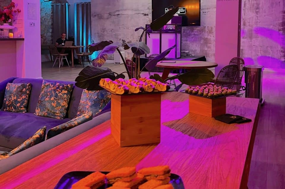 Vue sur un buffet dans le salle Lou,ge avec mets salés. Lumières tamisées rose