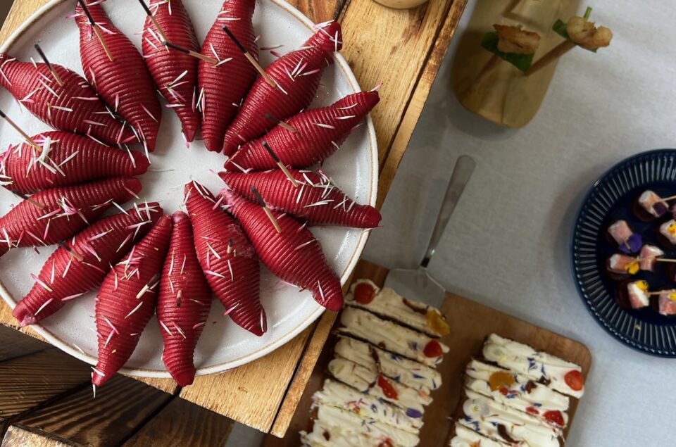 Exemple de mets : Pattes fourrées dans une assiette grise, Fromage crémeux aux fruits confis, verrines de légumes coupés en petits dés et brochettes de crevettes avec une feuille de basilique