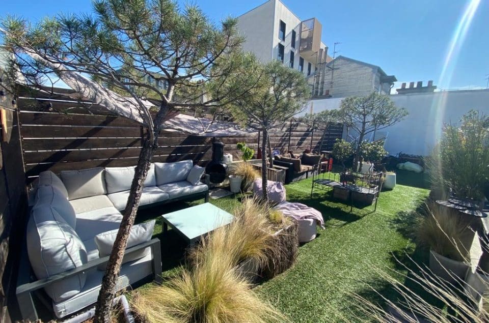 Vue d'angle du Rooftop avec canapé d'angle, fausse pelouse et arbre en pot